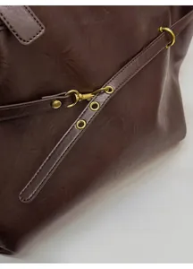 Detail of dark brown leather bag with golden metallic buckle and neat stitching