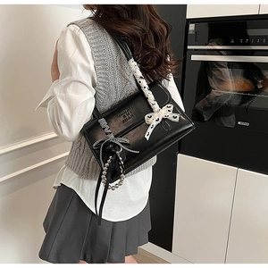 Detail of black leather shoulder bag with white lace bow and beaded charm on strap