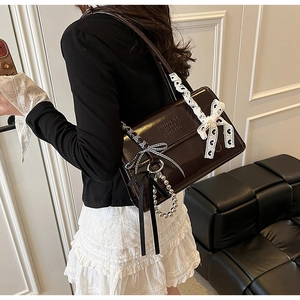 Détail du sac bandoulière marron foncé avec nœud en dentelle blanche et chaîne à perles argent