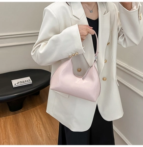 Pink minimalist crescent bag with silver zipper shown held by a model in a suit