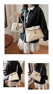 Detail of cream white envelope bag featuring woven strap and golden U-shaped metal buckle