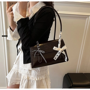 Close-up of brown patent leather bag featuring unique lace and checkered bow accents