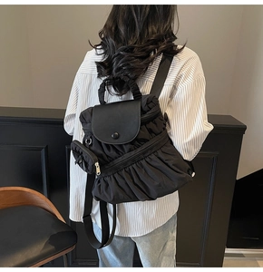 Macro detail of black pleated nylon backpack featuring a flap and detachable mini pouch