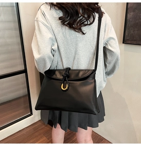 Close-up of black crossbody bag with golden U-shaped buckle and woven leather detail