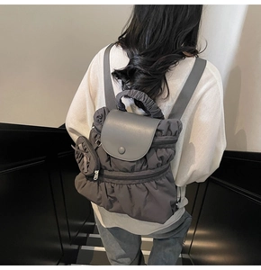 Detail of grey pleated backpack with leather flap and mini coin purse shown on model