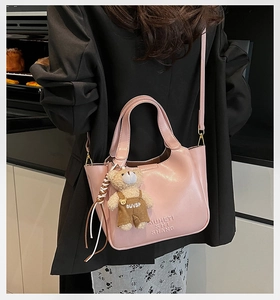 Pink faux leather bucket bag with cute bear charm worn as a stylish crossbody bag