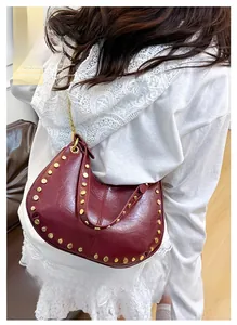 Detail of burgundy crescent bag with gold studs and metal chain on a model
