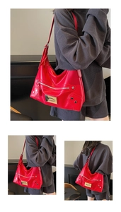 Détail d'un sac porté épaule rouge avec rivets argentés et plaque de marque en métal