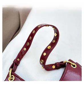 Close-up of wine red patent leather handle with golden rivets and metallic ring details