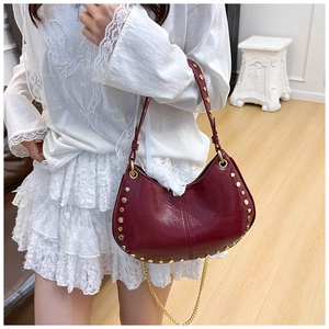 Detail of burgundy half-moon rivet bag with gold chain and studded leather texture