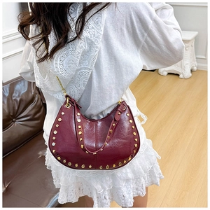 Detail of burgundy crescent shoulder bag featuring gold studs and glossy leather finish