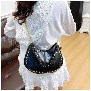Detail of black crescent shoulder bag with gold studs and chain strap on a model