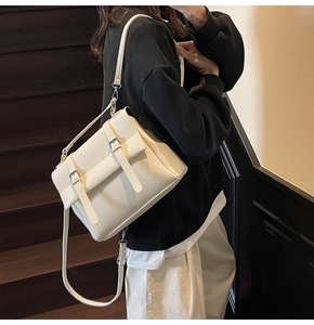 Detail of cream white leather messenger bag with dual belt buckle straps on front flap