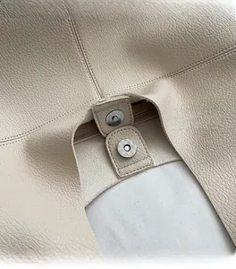 Detail of magnetic snap closure and pebble grain leather texture on beige tote bag