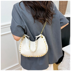 Detail of cream crescent hobo bag featuring gold rivet studs and metal chain strap