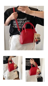 Close-up detail shot of the red litchi grain handbag with cute bear pendant and strap in daily scene.