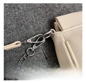 Dettaglio del gancio in metallo argento e catena sottile su borsa beige con cuciture rifinite