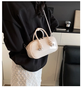 Vue latérale du petit sac à main crème en cuir verni porté par un mannequin en studio