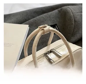 Détail d'un sac à main blanc crème montrant le fini brillant et les poignées nouées