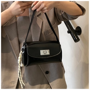 Détail d'un sac à bandoulière en cuir noir brillant avec un charm tressé blanc chic