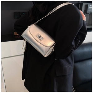 Gros plan d'un sac bandoulière argenté métallisé avec fermoir rotatif sur un blazer noir