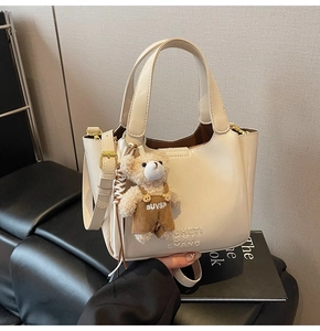 Detail der cremeweißen Beuteltasche mit geprägter Textur und süßem Bären-Anhänger