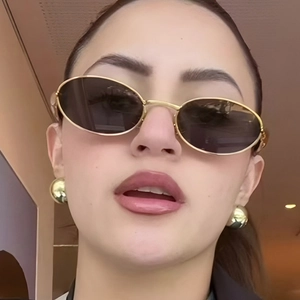Close-up of vintage oval gold metal sunglasses with dark lenses and matching gold earrings