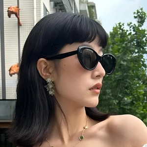 Modische schwarze Katzenaugen-Sonnenbrille für Damen mit Blumenohrringen und Goldhalskette