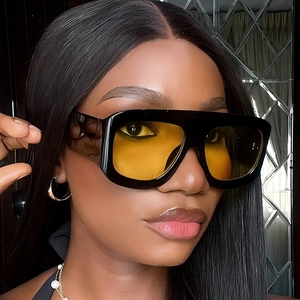 Quadratische Oversize-Sonnenbrille mit schwarzem Rahmen und gelben Gläsern am Modell