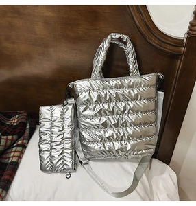 Detail view of silver quilted tote bag set with matching zipper pouch on white bedding