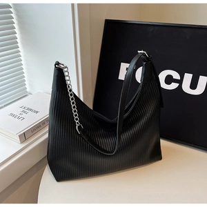 Gros plan d'un sac hobo noir avec texture plissée et chaîne argentée sur une table blanche
