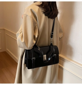 Détail d'un sac messager noir brillant avec fermoir argenté porté sur un trench-coat beige