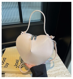 Detail of a pink heart-shaped crossbody bag featuring double zippers and glossy leather