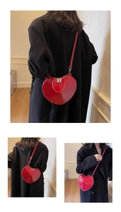 Macro view of a red heart-shaped patent leather crossbody bag with silver zippers