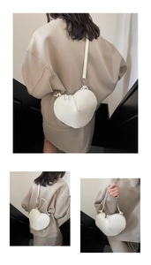 Detail of white heart-shaped leather crossbody bag with silver zipper and slim shoulder strap