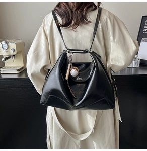 Detailed view of black leather tote bag with baseball charm and multifunctional straps