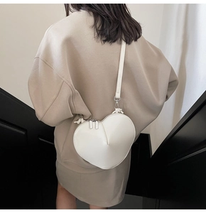 Detail of white heart-shaped leather crossbody bag with pleated texture and dual metal zippers