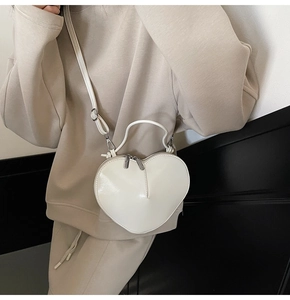 Macro detail of a white heart-shaped crossbody bag in glossy patent leather finish