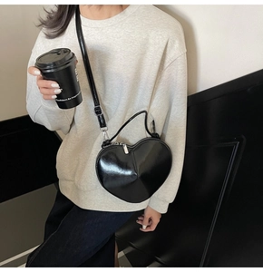 Detail of a black heart-shaped crossbody bag featuring a glossy finish and silver zipper