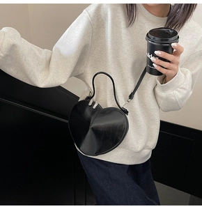 Detail shot of heart-shaped crossbody bag in glossy black leather with silver zipper