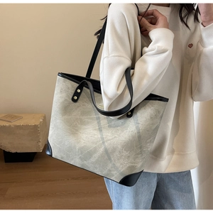 Dettaglio di una borsa tote marmorizzata con manici in pelle nera portata a spalla