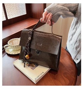 Detail einer dunkelbraunen Ledertasche mit Silberverschluss und gewebtem Anhänger