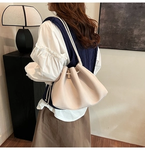 Detail of beige pleated leather bucket bag with drawstring closure on model's shoulder