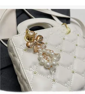 Détail d'un sac à main matelassé blanc avec breloque nœud doré et perles nacrées