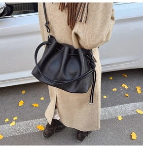 Detail showing black lychee textured bucket bag with drawstring closure on autumn street