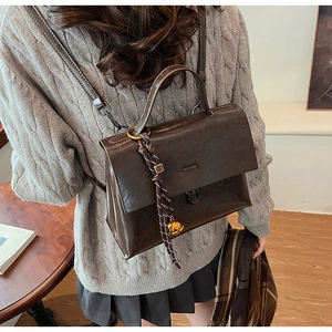 Detail der dunkelbraunen, glänzenden Lederrucksack-Handtasche mit goldener Schließe
