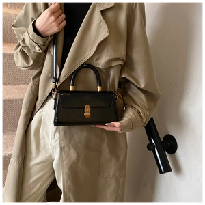 Close-up of black glossy leather crossbody bag with vintage gold metal lock on beige coat
