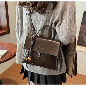 Detail der braunen Vintage-Handtasche mit silbernem Drehverschluss und Glockenanhänger