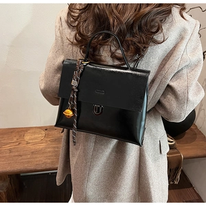 Detail einer schwarzen glänzenden Handtasche mit Metallschnalle und geflochtenem Anhänger