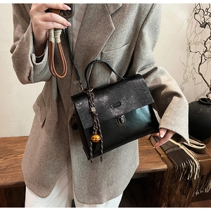 Detail einer schwarzen Handtasche mit zwei Texturen, Metallschloss und Goldglöckchen